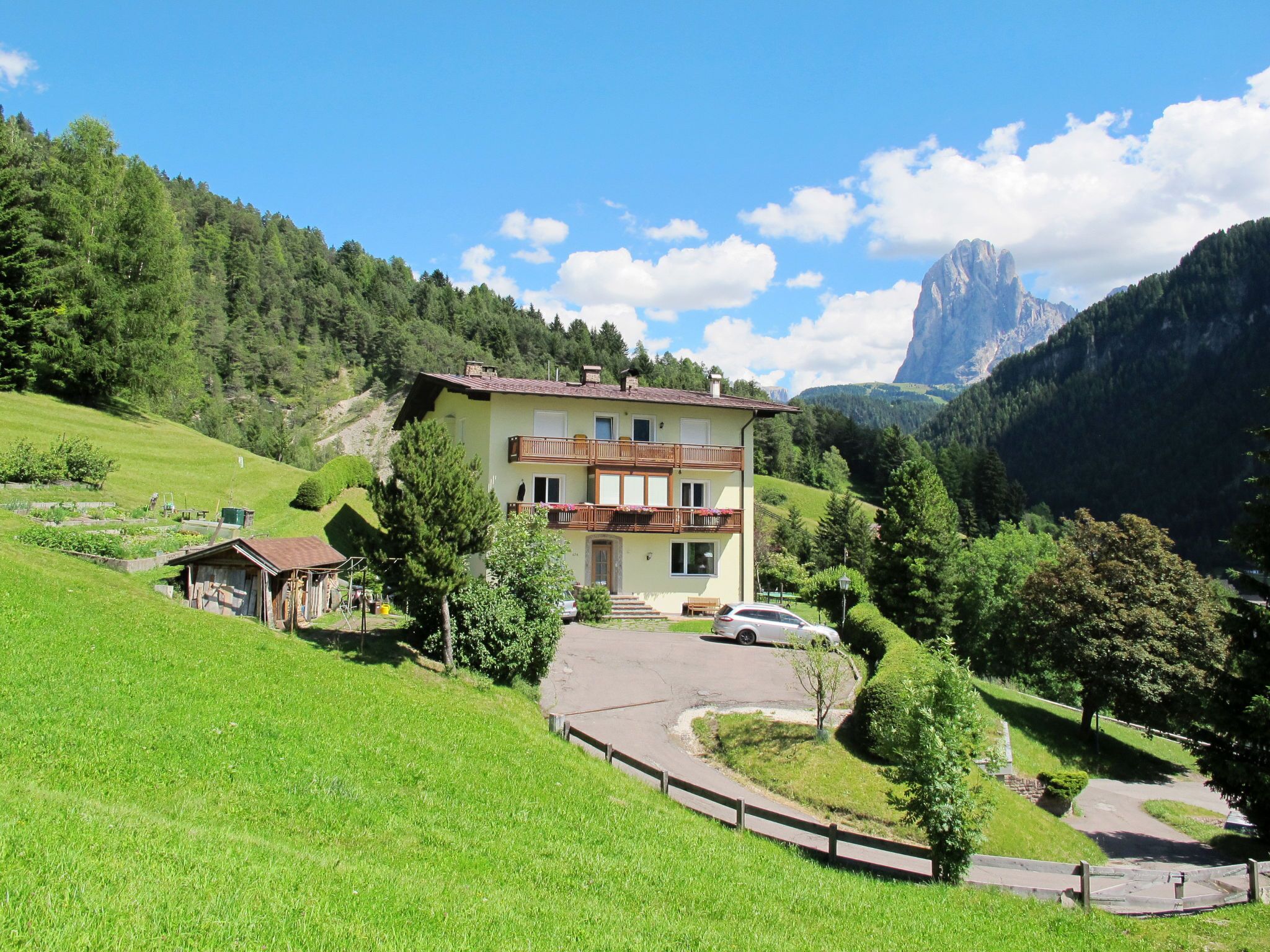 Une maison à deux étages dotée d’un balcon, entourée de collines verdoyantes et avec une montagne en toile de fond.