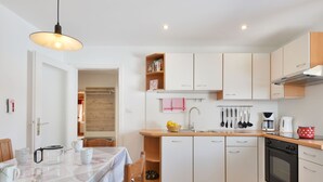 A compact kitchen with white cabinets, a wooden countertop, and a dining area with a table set for two. - Apartment Luca by Interhome (Ortisei St Ulrich)