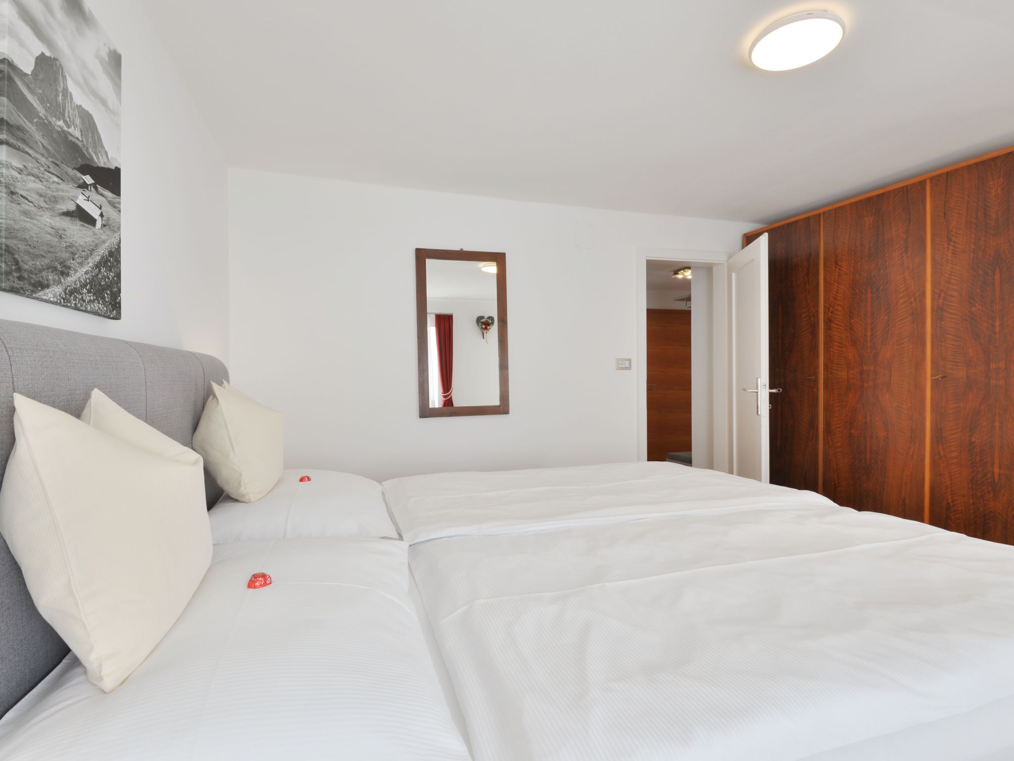 A bedroom with a large bed, a wooden wardrobe, a mirror, and a painting on the wall.