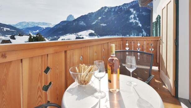 A balcony with a table set for two, a bottle of wine, and a bowl of snacks. - Apartment Luca by Interhome (Ortisei St Ulrich)