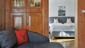 A cozy room with a wooden cabinet, a grey sofa with patterned cushions, and a bed with a grey headboard. - Apartment Luca by Interhome (Ortisei St Ulrich)