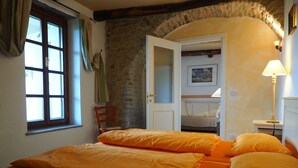 Una habitación con una cama, una silla, un ventanal y una puerta que da a otra estancia.