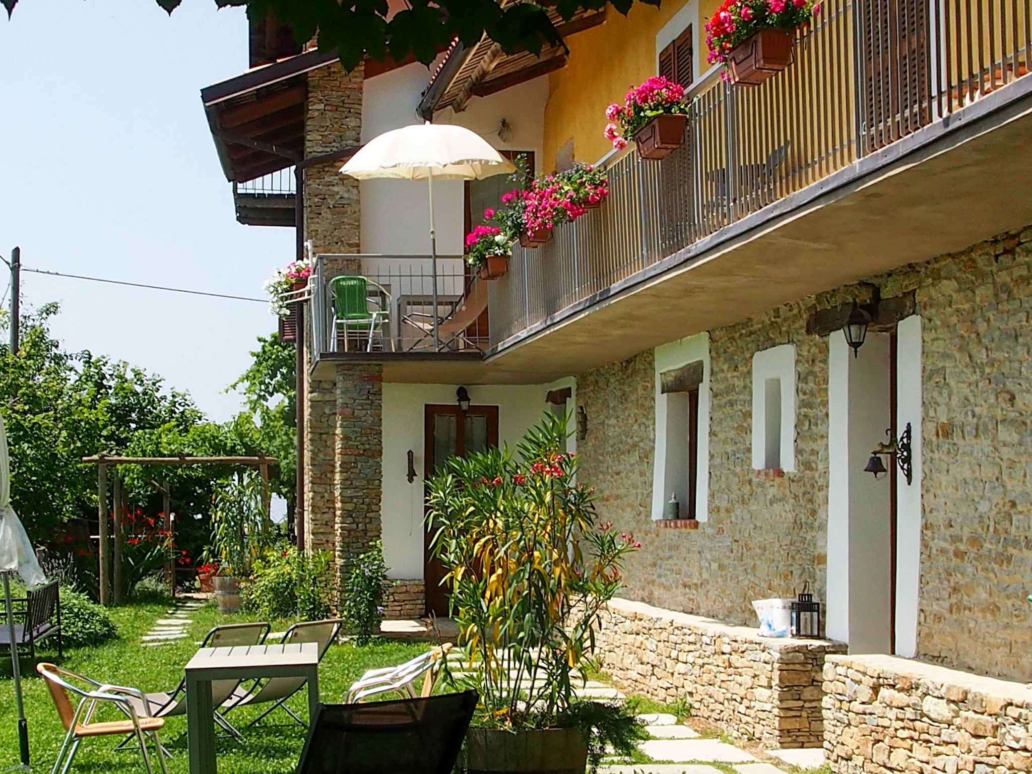 Edificio de piedra con un balcón decorado con flores, una mesa y sillas afuera, y un jardín.