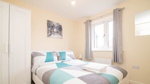 A bedroom with a bed, a wardrobe, a window with curtains, and a wall-mounted picture. - Quiet and Lovely 3-bed house parking and garden (Wolverhampton)