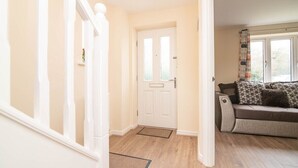 A hallway with a white door, a wooden floor, and a sofa with patterned cushions. - Quiet and Lovely 3-bed house parking and garden (Wolverhampton)