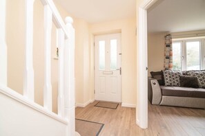 A hallway with a white door, a wooden floor, and a sofa with patterned cushions.