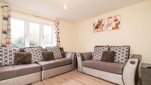 A modern living room with a sectional sofa, a small table, and abstract wall art. - Quiet and Lovely 3-bed house parking and garden (Wolverhampton)
