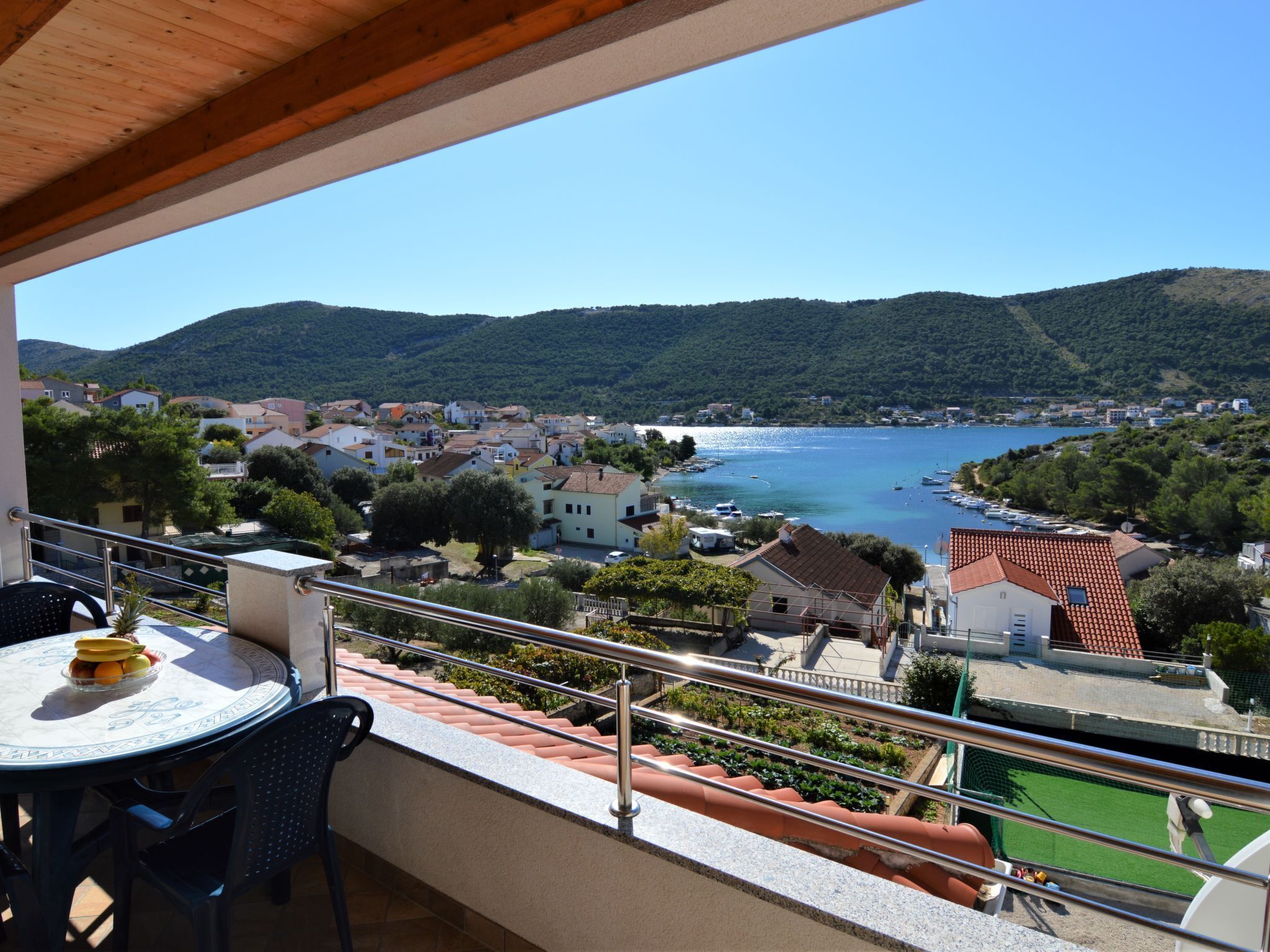 Un balcon avec une table et des chaises, donnant sur une ville côtière avec ses maisons et sa baie.