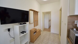 Une chambre d’hôtel moderne équipée d’un téléviseur à écran plat posé sur un meuble blanc, d’une armoire en bois, d’un four à micro-ondes et d’une salle de bain avec un lavabo et un miroir.