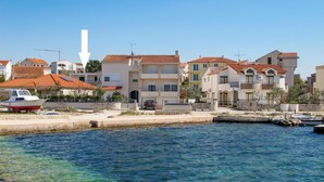 A coastal town with buildings featuring red-tiled roofs, a marina with boats, and clear blue water. - Katarina 3 by Interhome (Šibenik)