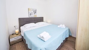 Un lit bien fait, recouvert d’une couvre-lit bleu clair et agrémenté d’oreillers blancs, une table de chevet avec une lampe, et une œuvre d’art accrochée au mur au-dessus du lit.