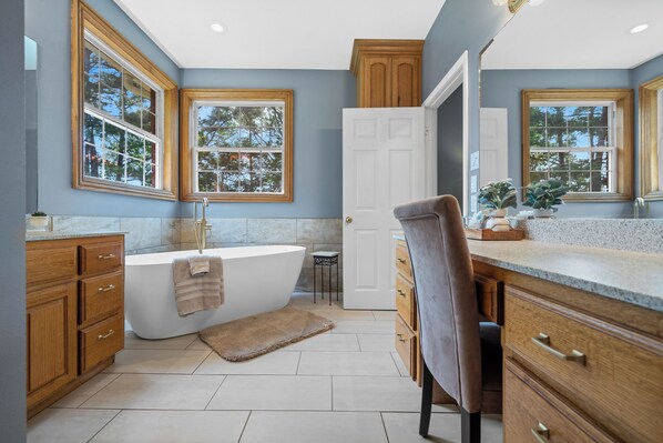 A modern bathroom with a freestanding bathtub, wooden cabinetry, and large windows.