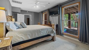Une chambre à coucher comprenant un lit, un bureau, une chaise, un téléviseur et une fenêtre donnant sur une structure en bois.