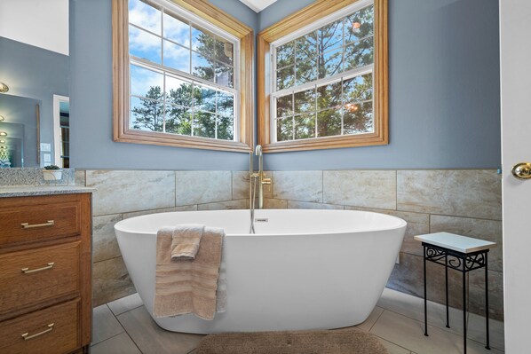 A modern bathroom with a freestanding bathtub, wooden window frames, and a marble countertop.