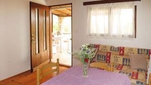 A room with a wooden floor, a purple table with a vase of flowers, a wooden chair, a patterned sofa, and a window with sheer curtains. - Kalebica by Interhome (Pašman/Pašman)