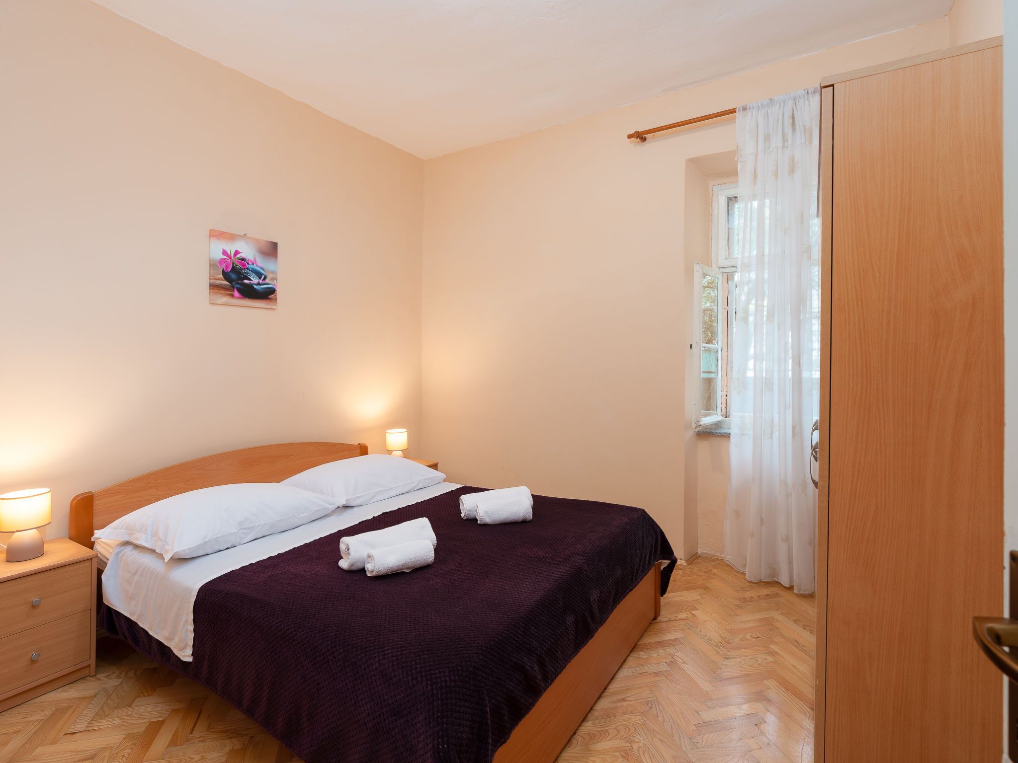A bedroom with a bed, nightstands, a wooden wardrobe, and a window with curtains.