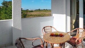 Ein Balkon mit einem runden Tisch und vier Korbstühlen, jeder mit einer Kissenauflage. Auf dem Tisch stehen drei Gläser.