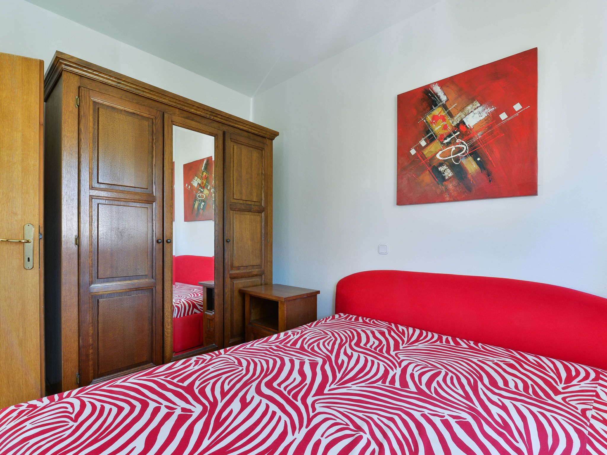 Un dormitorio con cama, armario y pared roja.