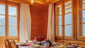 Una sala da pranzo in legno con una baita, un tavolo apparecchiato per due, ampie finestre e vista sulle montagne.