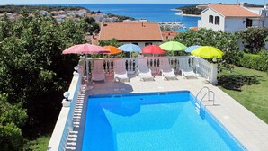 A swimming pool with lounge chairs and umbrellas, surrounded by greenery and overlooking a coastal town. - Villa Ursa by Interhome (Pula)