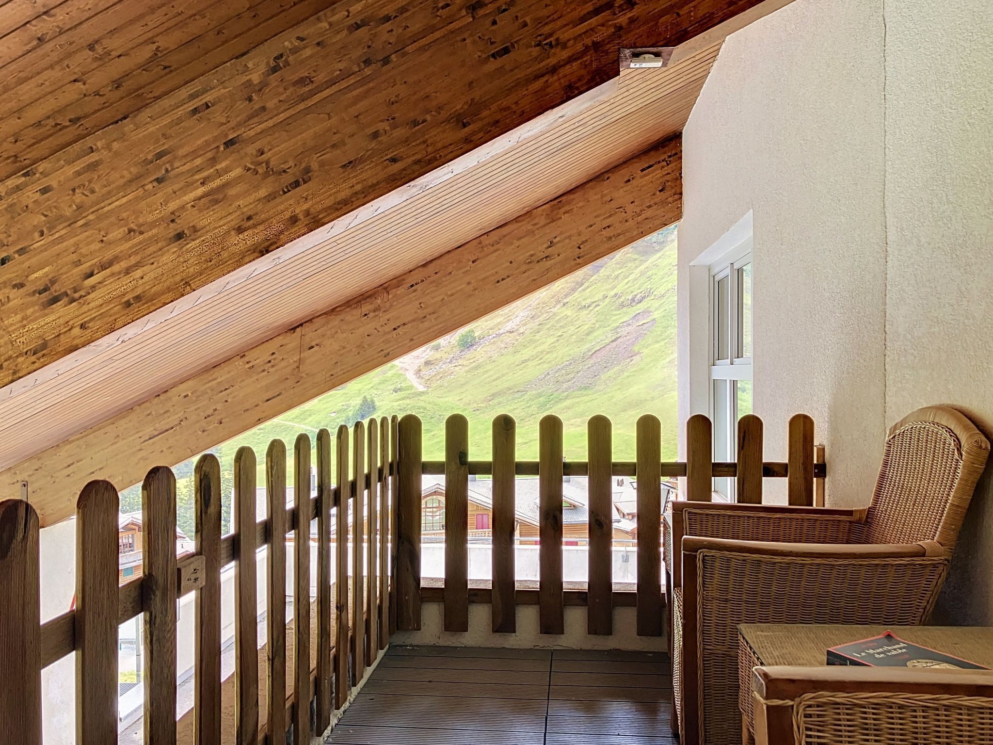 Ein Holzbalkon mit Holzwertlauf, ein Korbstuhl und Blick auf eine grüne Landschaft.