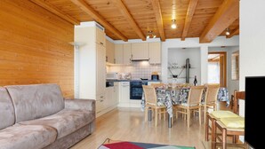 Een gezellige woonkamer met een bank, een eettafel met stoelen en een keuken op de achtergrond.