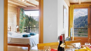 Een kamer met een bed, een gedekte tafel en uitzicht op bergen door het raam.