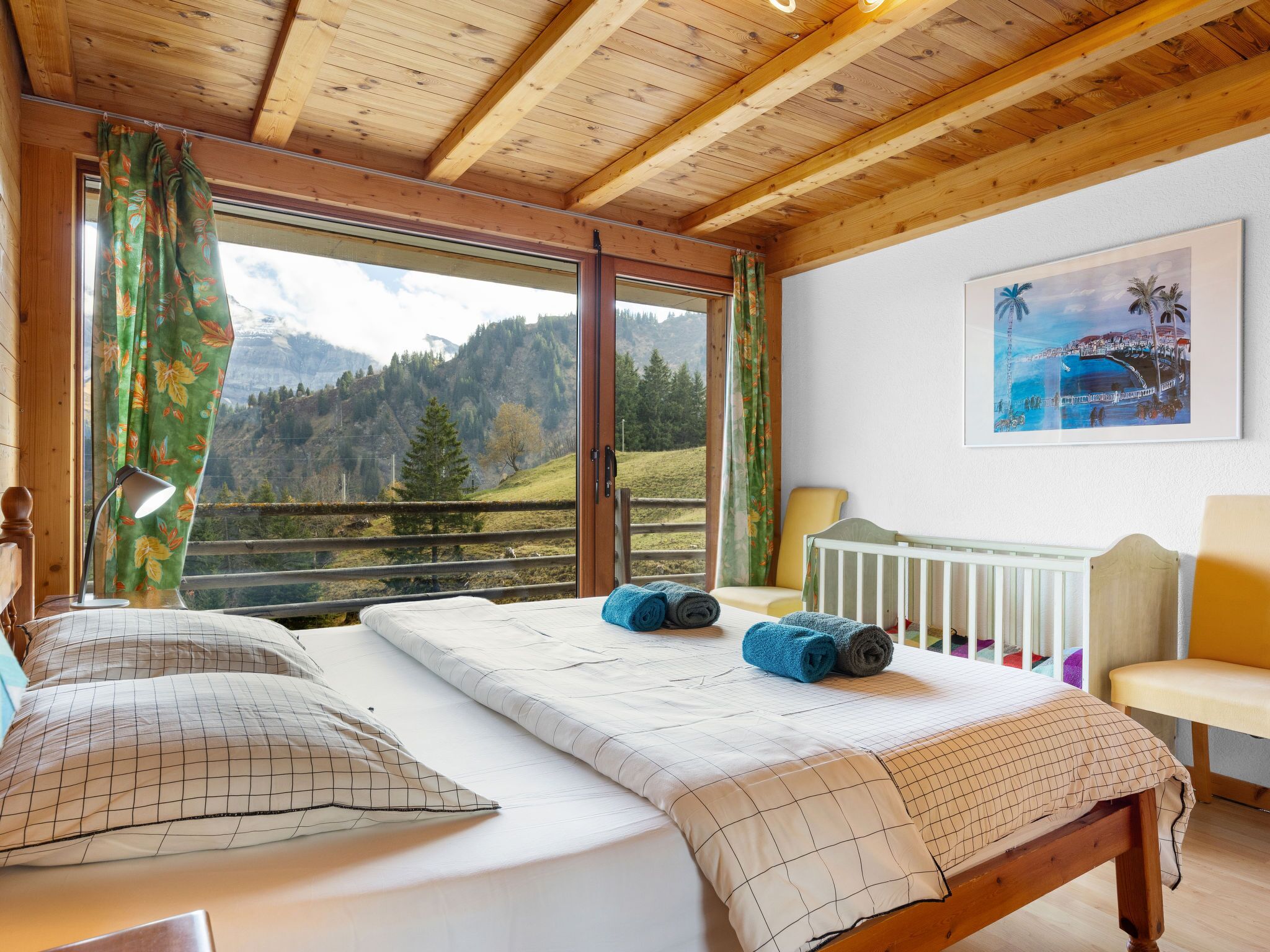 Une chambre à coucher avec un lit, un berceau, une fenêtre donnant sur les montagnes et un tableau accroché au mur.