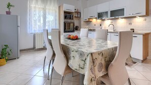 A modern kitchen with white cabinets, a dining table with a floral tablecloth, and chairs. - Apartment Cekić by Interhome (Rovinj)