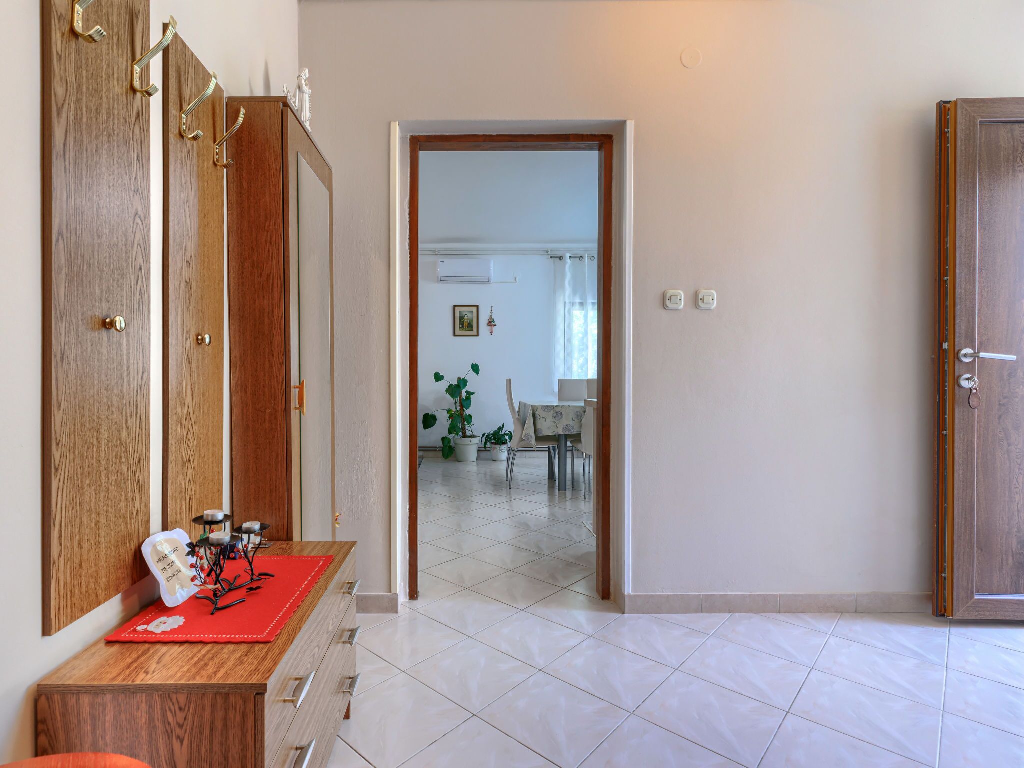 Un corridoio con una porta in legno, un tappetino rosso e un tavolino con oggetti decorativi.