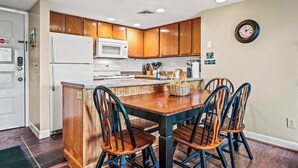 A kitchen with wooden cabinets, a white refrigerator, a microwave, and a dining area with a wooden table and chairs.