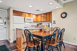 A kitchen with wooden cabinets, a white refrigerator, a microwave, and a dining area with a wooden table and chairs.