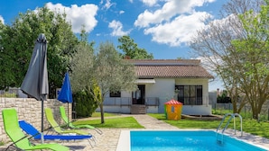 A swimming pool with lounge chairs, a small playhouse, and a house with a tiled roof.