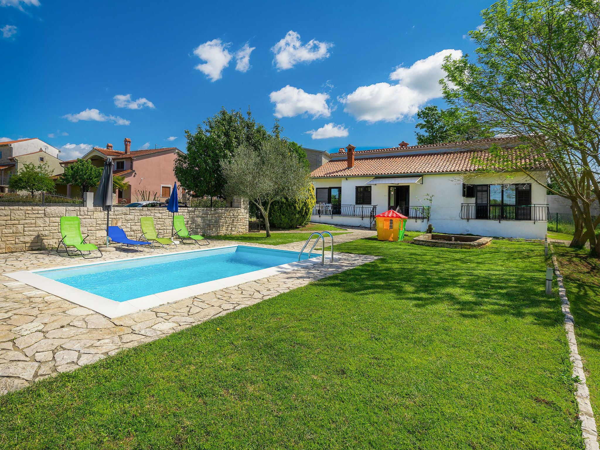 A swimming pool with lounge chairs, a small playhouse, and a well-maintained lawn.