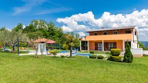 Ein zweistöckiges Haus mit Swimmingpool, umgeben von einem gepflegten Rasen und Bäumen.