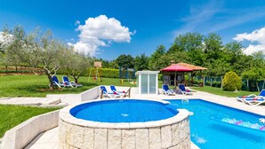 Ein Schwimmbecken mit Liegestühlen und einem Whirlpool, umgeben von einem gepflegten Rasen und Bäumen.