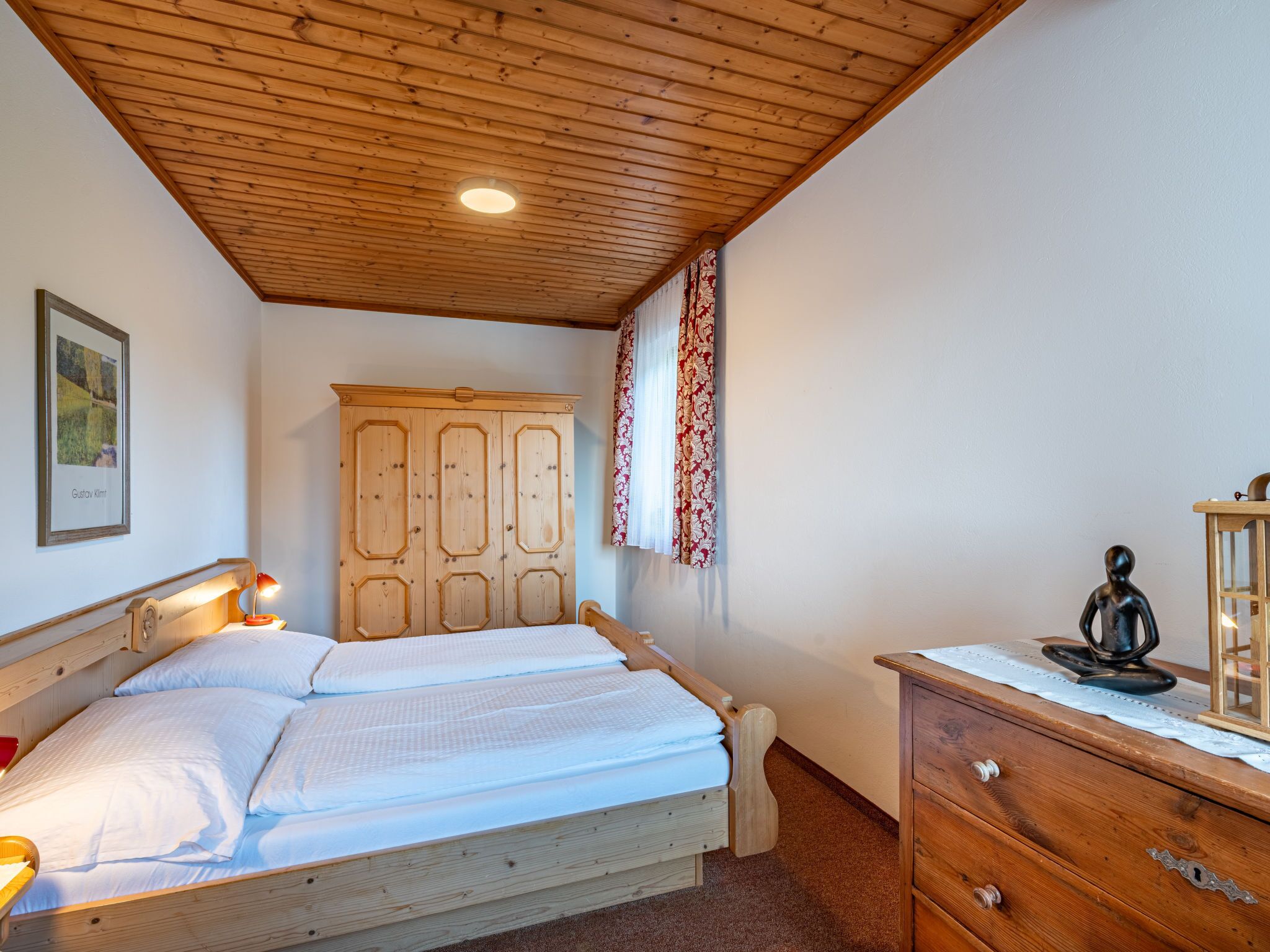 Un dormitorio con techo de madera, una cama con ropa de cama blanca, un aparador de madera y un armario con puertas.