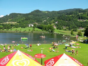 Un resort junto al lago con zonas verdes, sombrillas y gente relajándose junto al agua.