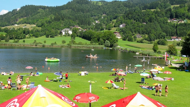 Un resort sul lago con aree verdi, ombrelloni e persone che si rilassano sulla riva.