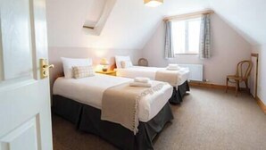 Une chambre d’hôtel avec deux lits, une fenêtre avec des rideaux, une chaise et une petite table avec une lampe.