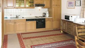 Een keuken met houten kastjes, een fornuis, een spoelbak en een magnetron.