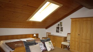 A bedroom with a sloped ceiling, a skylight, a bed with multiple pillows, a bedside table with a lamp, a wooden wardrobe, and a chair. - Lassnig by Interhome (Arriach)