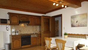 A kitchen with wooden cabinets, a microwave, a coffee maker, and a dining area with a table and chairs. - Lassnig by Interhome (Arriach)