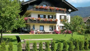 A two-story building with balconies adorned with flowers, a well-maintained lawn, and a mountain in the background. - Lassnig by Interhome (Arriach)