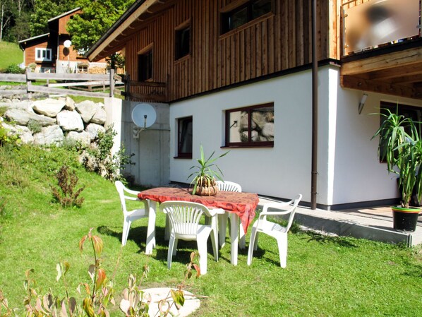 Una casa de madera con balcón, una mesa de comedor con sillas y una planta en maceta.