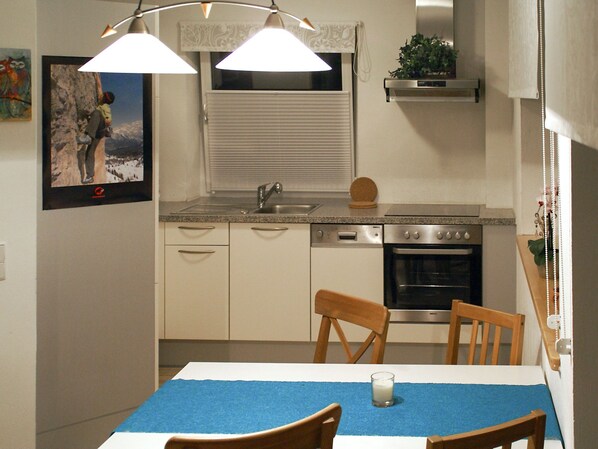 A compact kitchen with a sink, dishwasher, and oven. There is a dining table with chairs and a blue placemat.