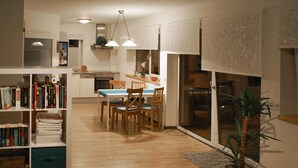 Amplia sala de estar con suelo de madera, una mesa de comedor con sillas, una estantería y una planta en maceta.