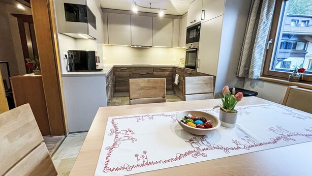 Una cocina moderna con armarios blancos, un microondas y una estufa. Hay una mesa de comedor con un mantel individual y un cuenco de fruta.