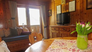 Un acogedor interior de cabaña con una mesa de comedor de madera, un sofá y un televisor.