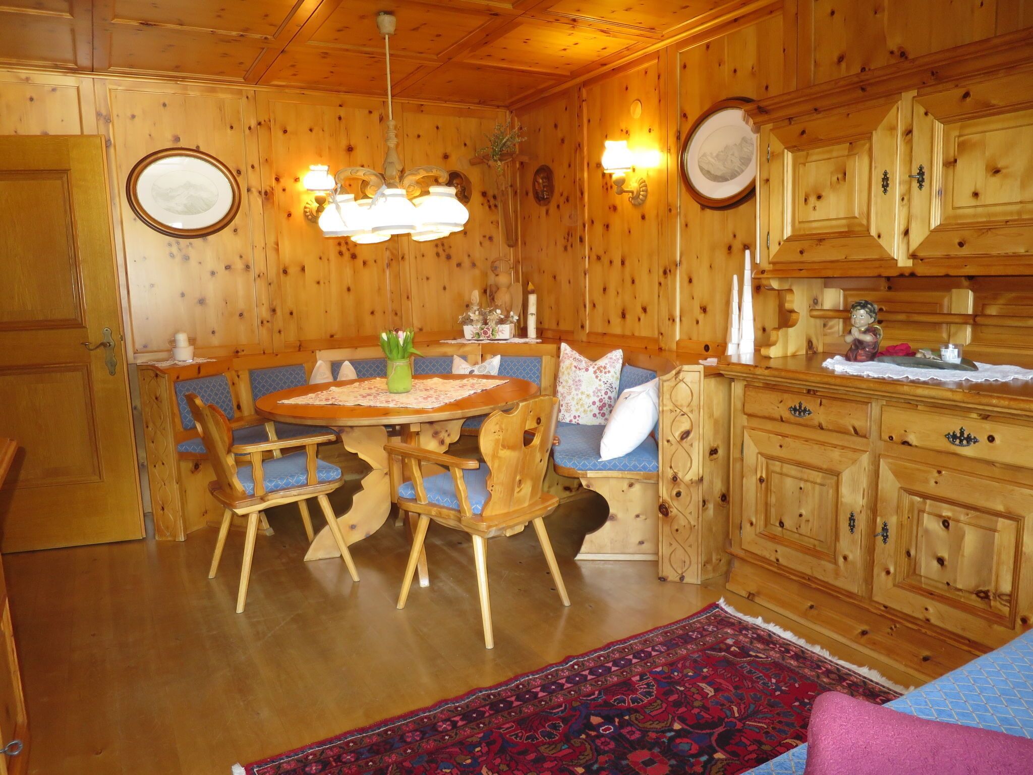 Ein Holzinterieur mit einem runden Esstisch, blau gepolsterten Stühlen, einer Bank und einem gemusterten Teppich.